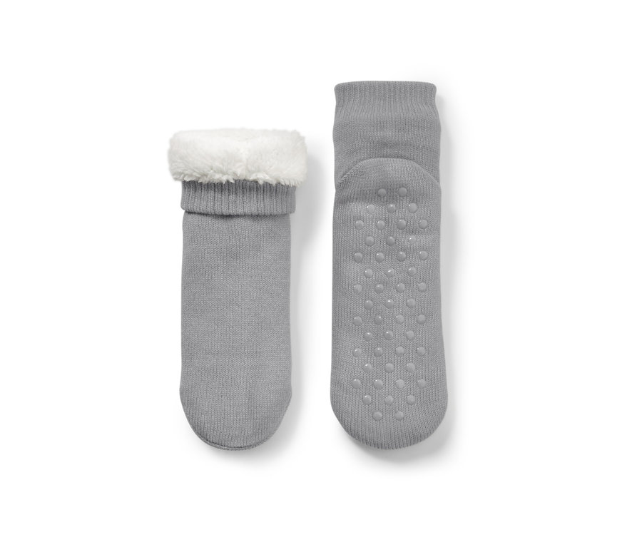 Zwei graue Hausschuh-Socken, eine mit weißem Plüschrand, die andere mit Antirutsch-Noppen.