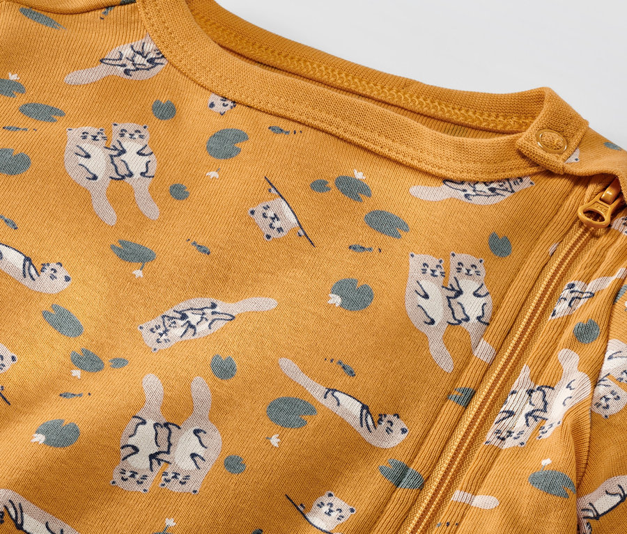 Detailansicht eines gelben Baby-Schlafanzugs mit Reißverschluss und Otter/Gans-Muster.