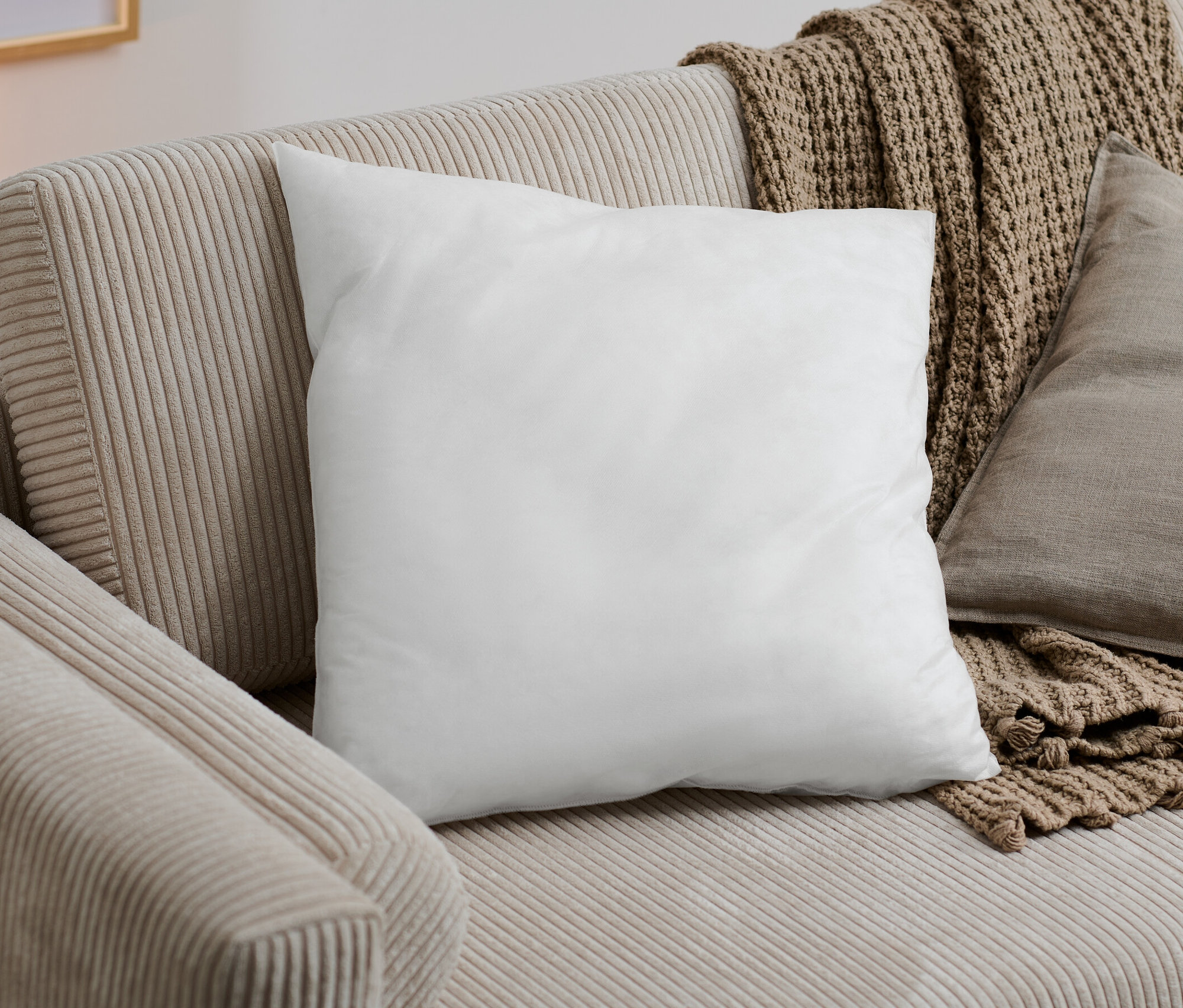 Weißes Füllkissen auf einem beigen Sofa mit einer braunen Decke.