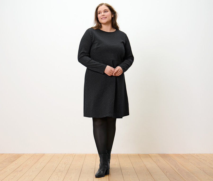 Frau steht und trägt ein glitzerndes Jacquard-Kleid.