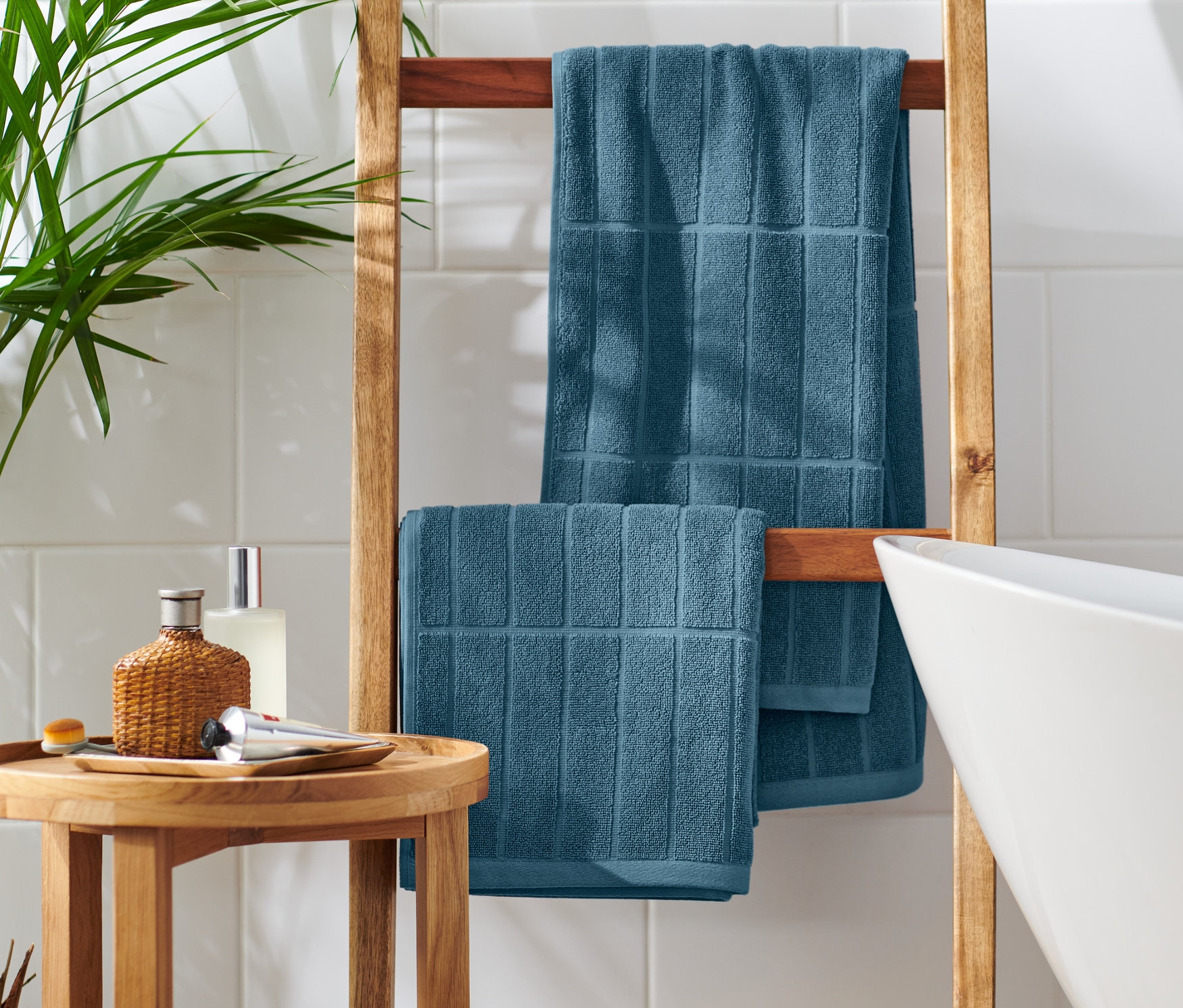 Zwei blaue Premium-Handtücher hängen auf einer Holzleiter neben einer weißen Badewanne.
