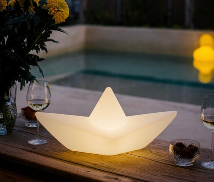 Goodnight Light LED-Leuchte »Boot« auf einem Holztisch neben Weingläsern und Blumen.