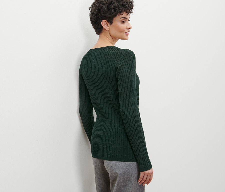 Frau im Profil trägt einen grünen Zopfstrickpullover.