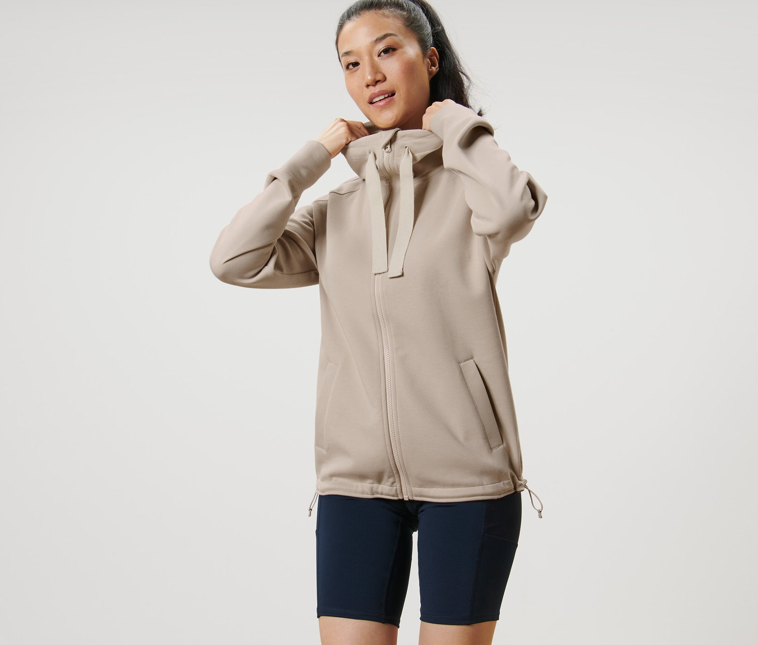 Frau richtet beige Kapuzen-Sweatjacke.