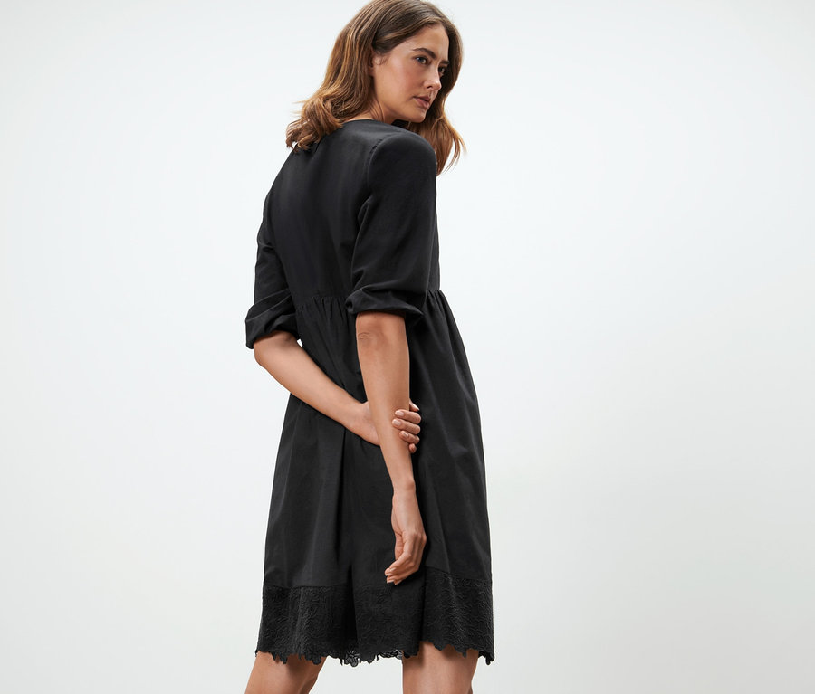 Frau posiert in schwarzem Webkleid mit Stickerei.