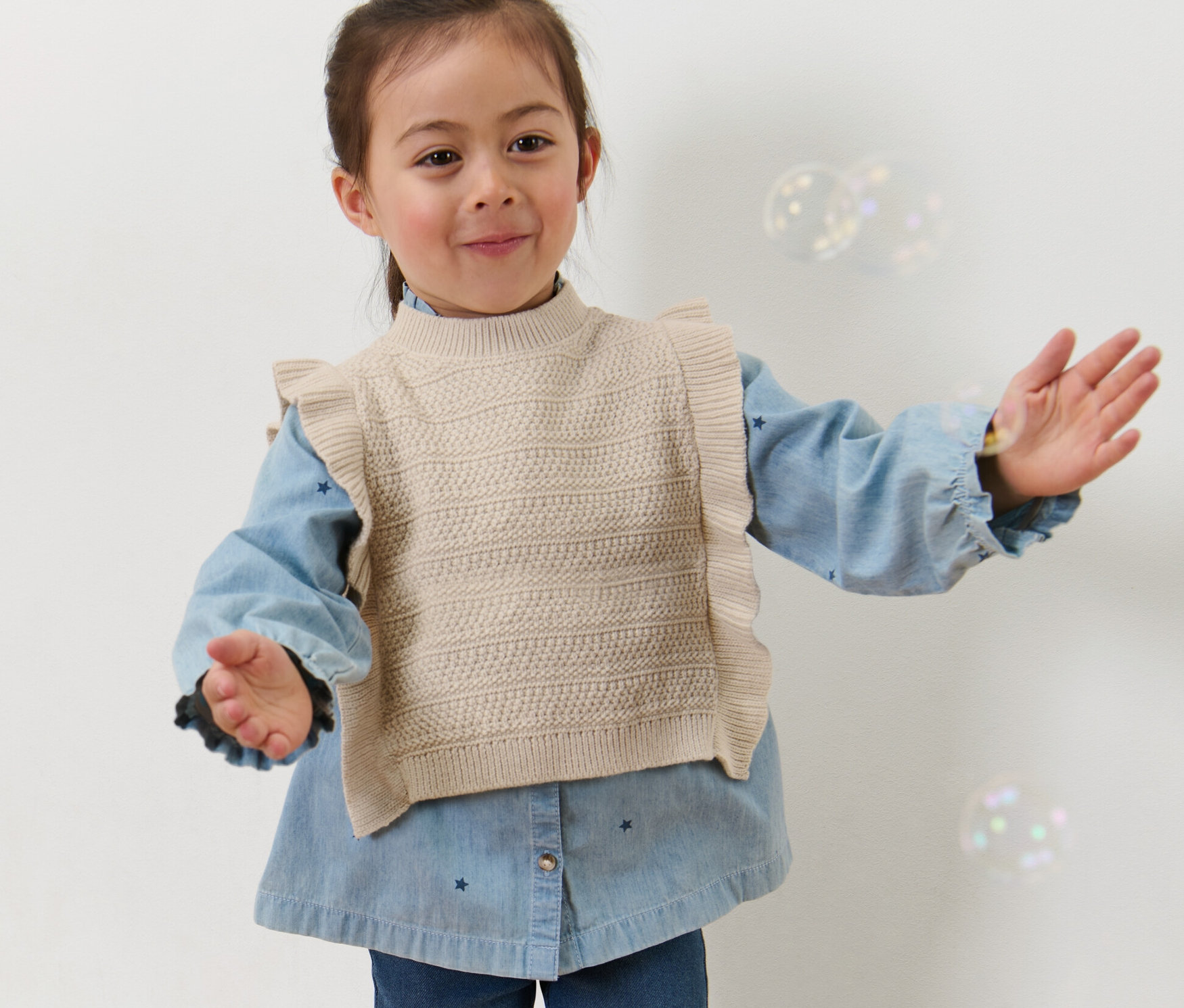 Mädchen in Kinder-Strickpullunder posiert mit ausgestreckten Armen.