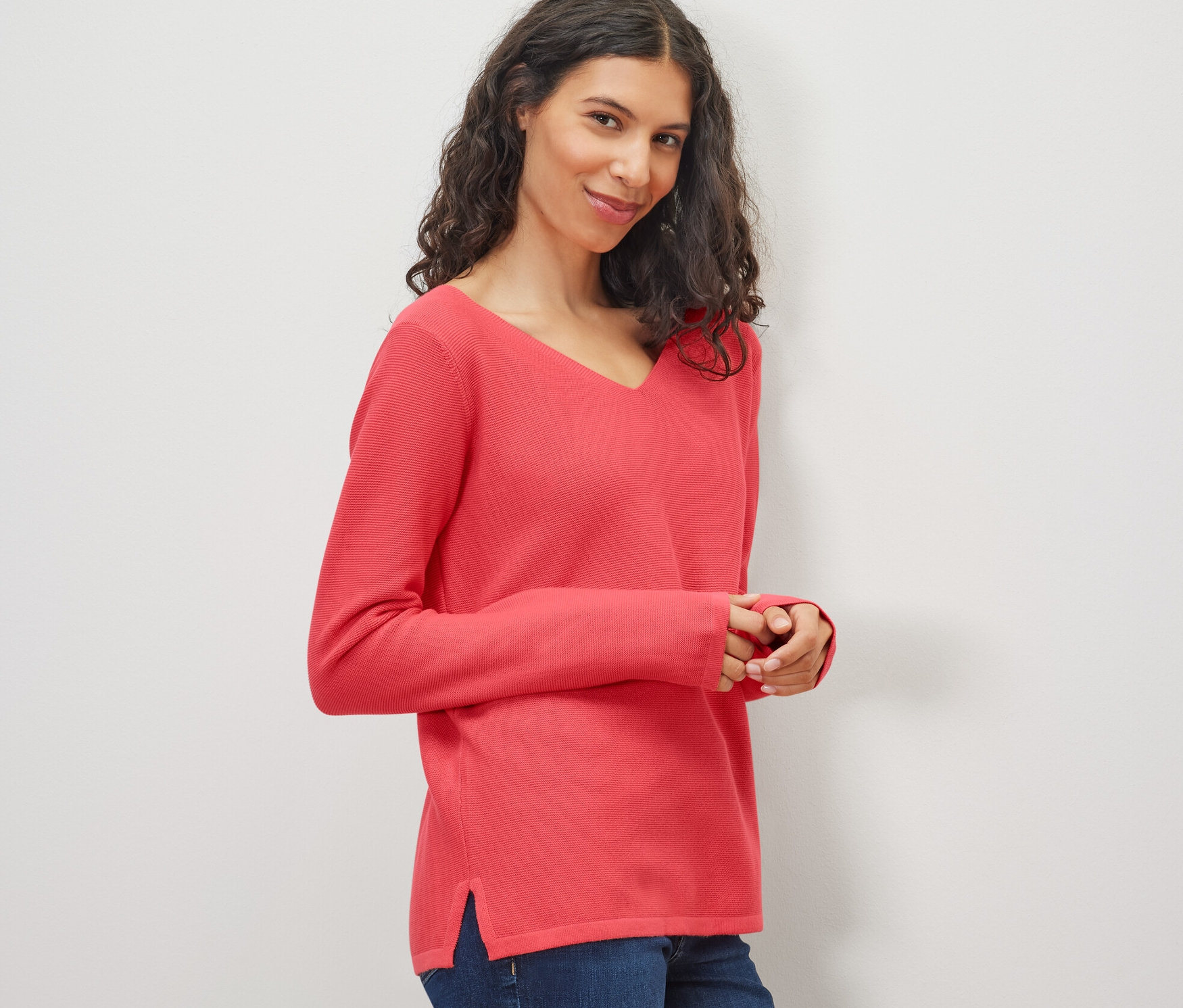 Frau trägt korallenfarbenen Strickpullover und Jeans.
