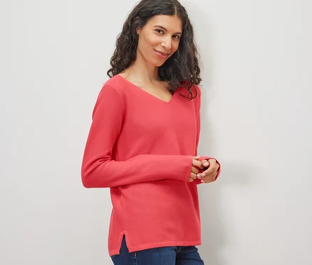 Frau trägt korallenfarbenen Strickpullover und Jeans.