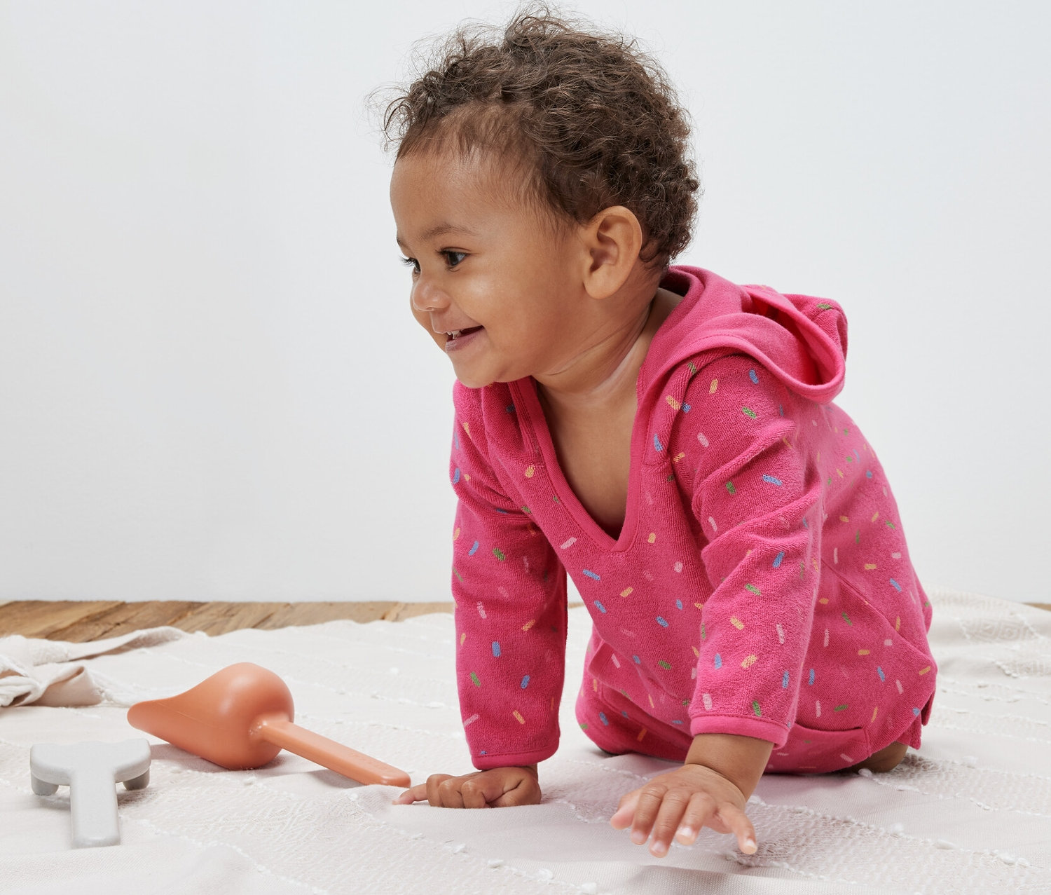 Kleinkind krabbelt auf einer Decke und trägt einen pinken Frottierponcho.