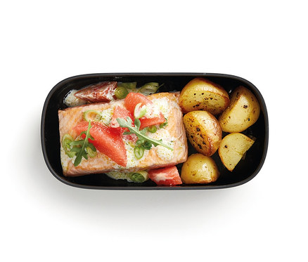 In einer schwarzen Lunchbox befindet sich Lachs mit Kartoffeln.