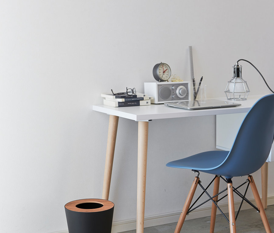 Schreibtisch mit Büchern, Brille, Radio, Lampe und Tablet, daneben ein schwarzer, runder YAMAZAKI Mülleimer »RIN«.