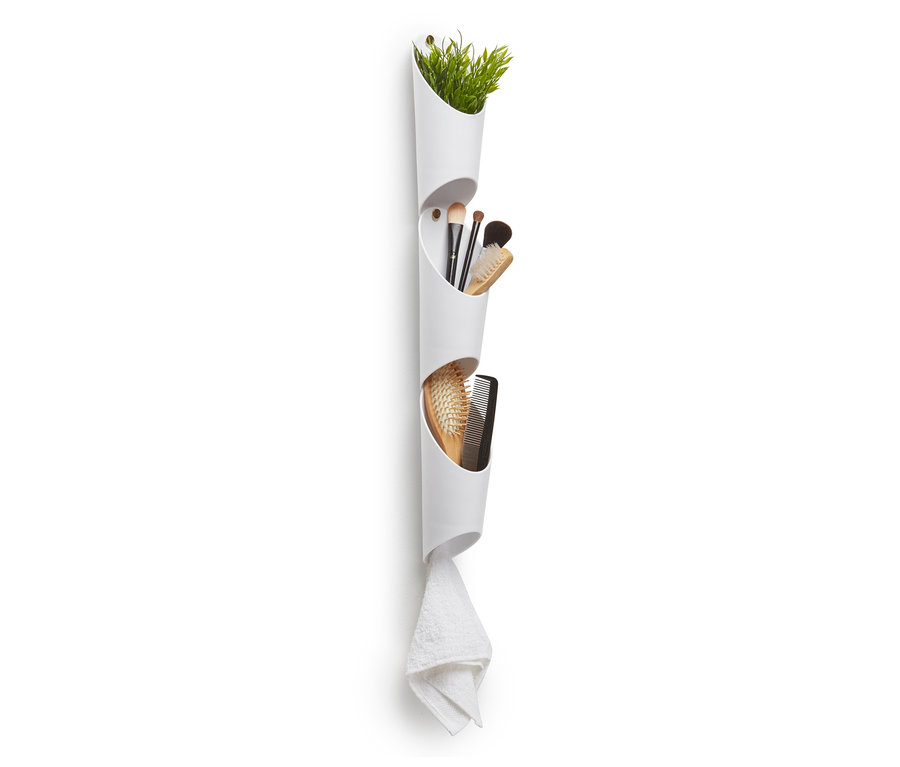 Eine weiße Wandvase mit drei Fächern enthält eine Pflanze, Schminkpinsel und Kämme. Ein Handtuch hängt unten.