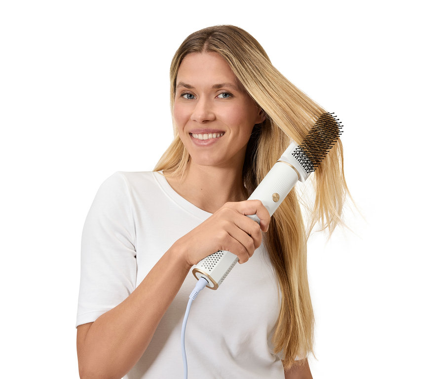 Frau stylt ihr blondes Haar mit einer Warmluftbürste.