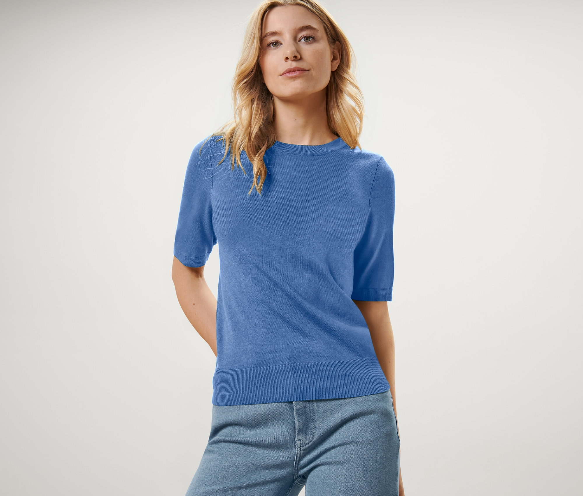 Frau trägt einen blauen Feinstrickpullover und Jeans.