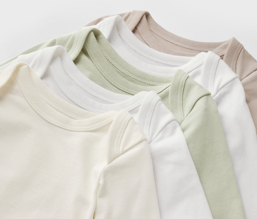 Detailansicht von fünf Baby-Bodys mit Mitwachsfunktion in Beige-, Weiß- und Hellgrüntönen.