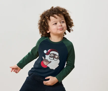 Junge mit lockigen Haaren trägt ein blaugrünes T-Shirt mit einer Abbildung von Santa Claus.