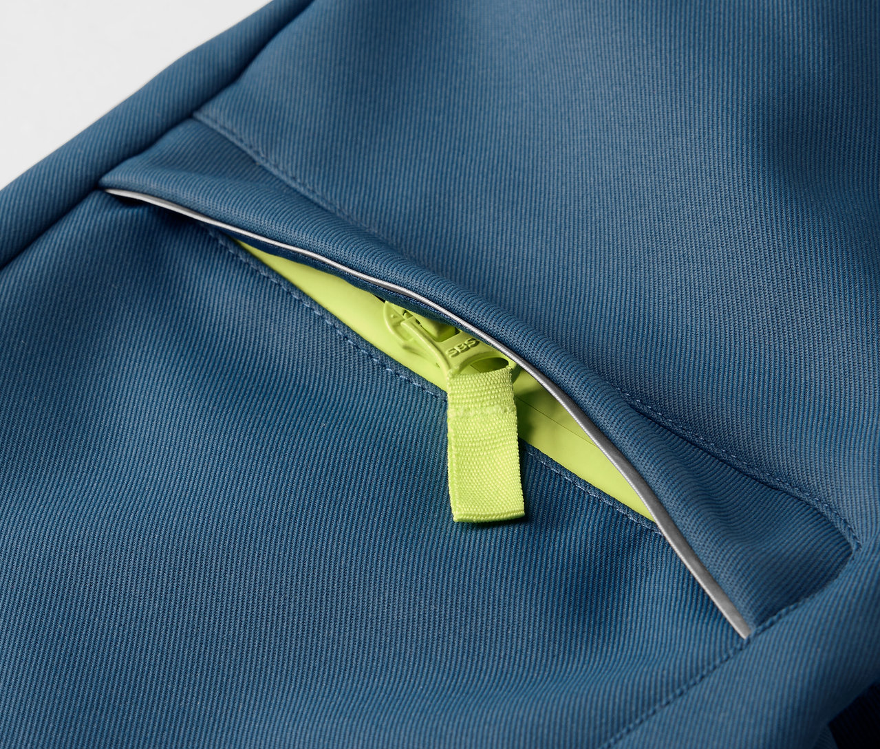 Detailaufnahme einer Kinder-Softshellhose mit neon-grünem Reißverschluss.