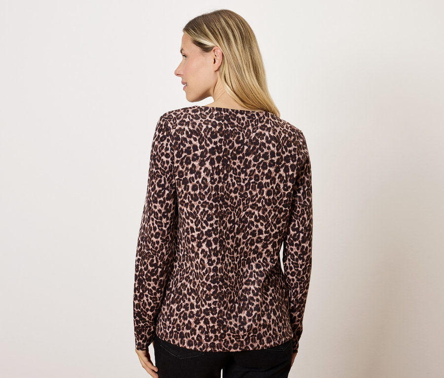 Blonde Frau mit brauner Bluse mit Tiermuster, mit dem Rücken zur Kamera.