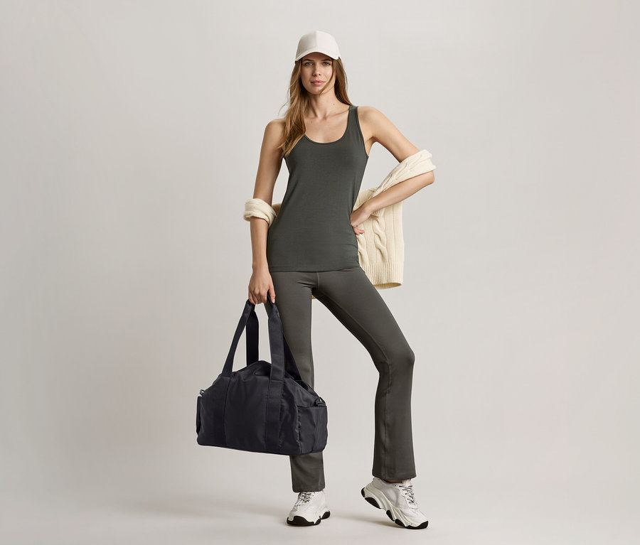 Frau in olivgrünem Top und Bodyforming-Sporthose, hält schwarze Sporttasche.