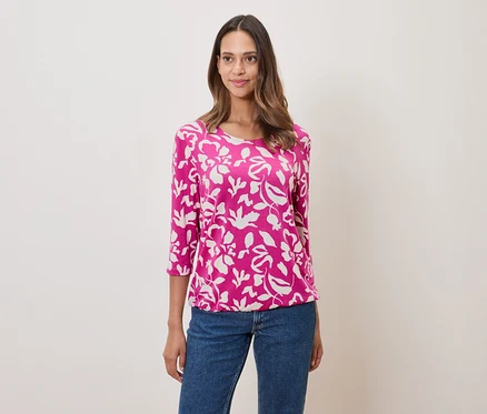 Frau trägt ein pinkes, blumengemustertes Oberteil und Jeans.