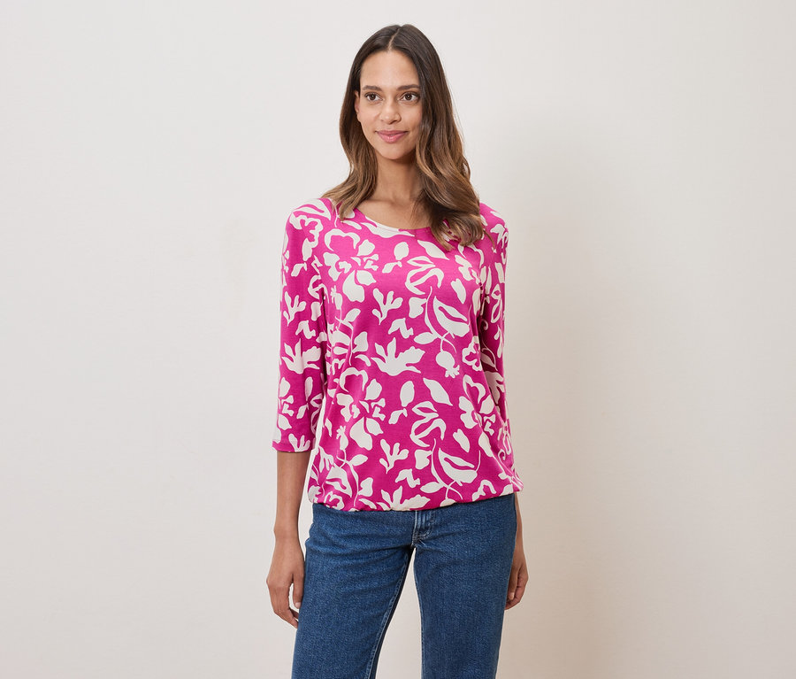 Frau trägt ein pinkes, blumengemustertes Oberteil und Jeans.