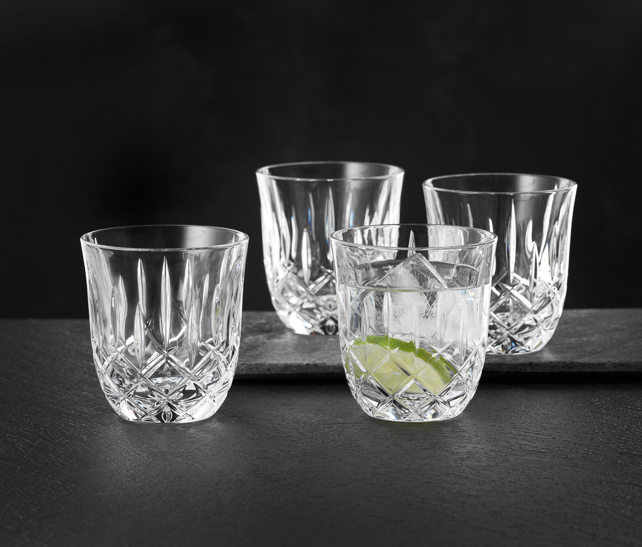 Vier Nachtmann Cappuccinogläser »Noblesse«, eines mit Eiswürfeln und Limette, auf einer dunklen Oberfläche.
