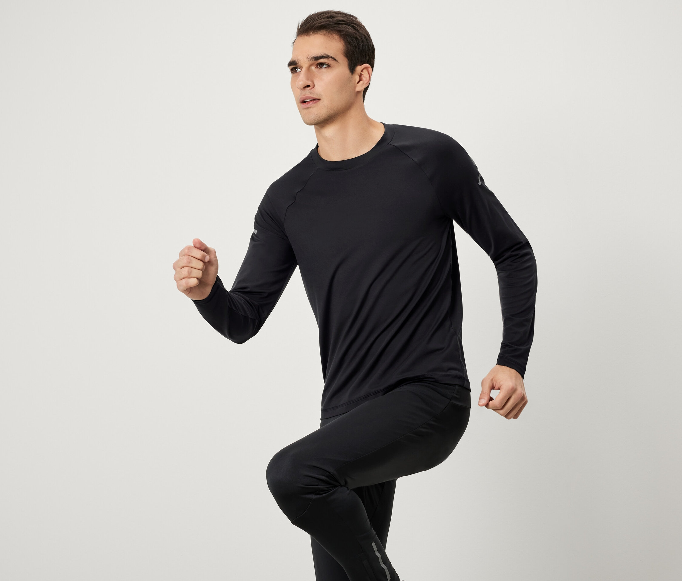 Mann in schwarzer Sportbekleidung mit langärmligem Oberteil und Hosen beim Laufen.