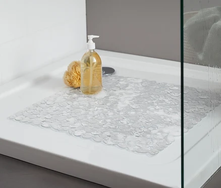Duschwanne mit transparenter Duschwanneneinlage. Auf der Wanne liegen ein gelber Badeschwamm und eine Flasche mit Pumpspender.