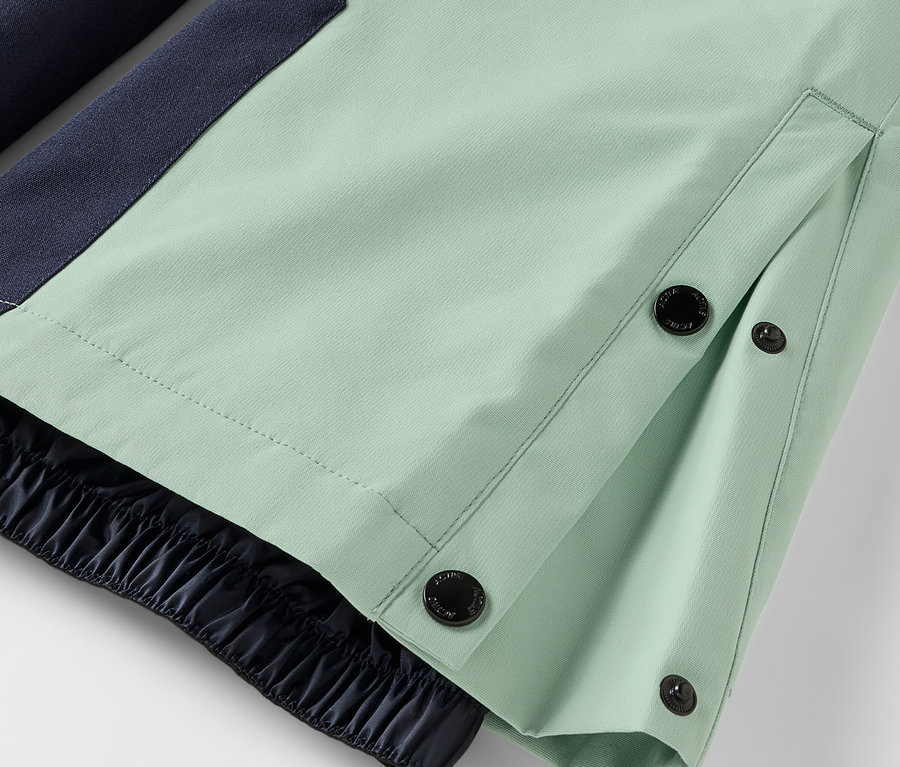 Detail einer hellgrünen Hose mit Knopfverschluss und elastischem Saum.
