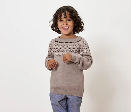 Lächelnder Junge in braunem Pullover mit Muster und blauen Hosen.