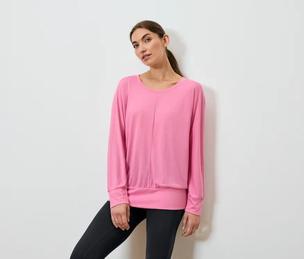Frau posiert in einem pinkfarbenen, langärmeligen Sportoberteil und schwarzen Leggings.