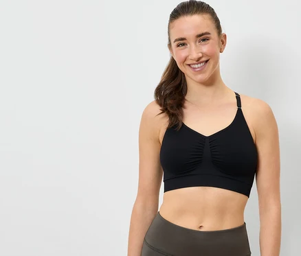 Lächelnde Frau trägt einen schwarzen Sport-BH und graue Leggings.