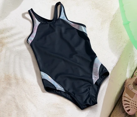 Kinder-Badeanzug liegt auf Sand neben Sandalen und einem grünen Schwimmreifen.