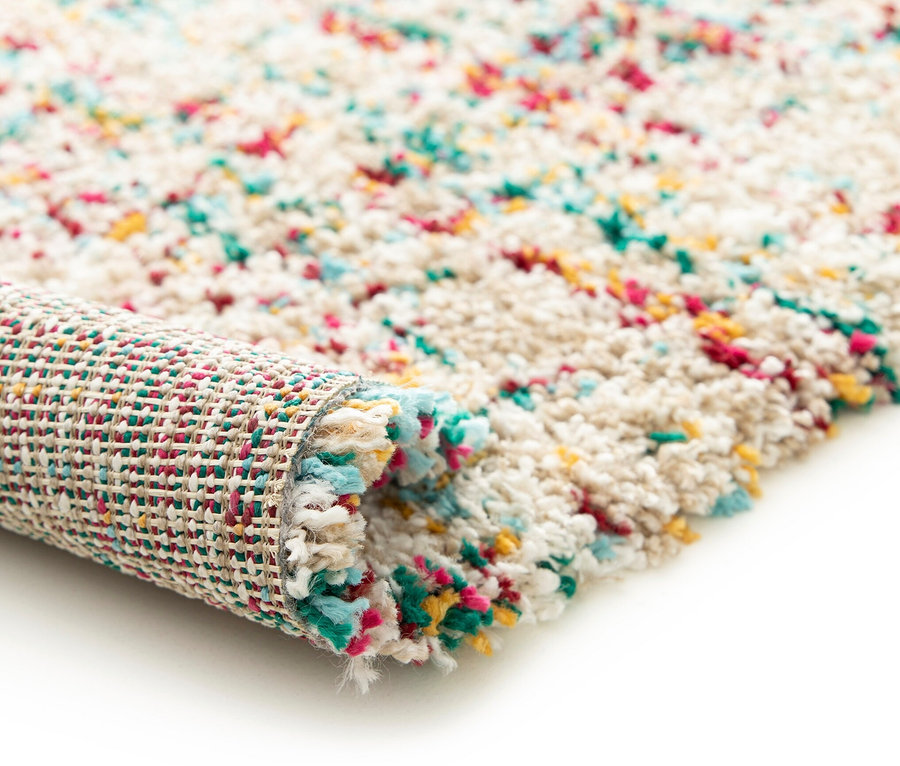 Nahaufnahme eines beigen, zotteligen Teppichs »Relic« mit gedämpften Pastellfarben, teilweise aufgerollt.