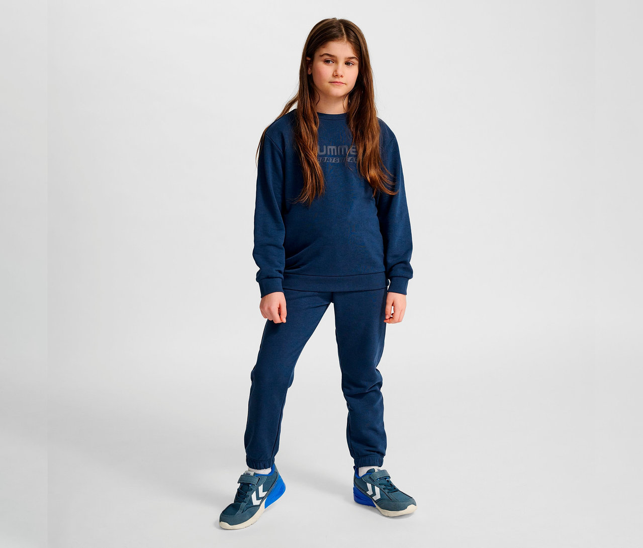 Mädchen trägt blaues Hummel HMLJR Base-Sweatshirt und blaue Jogginghose.
