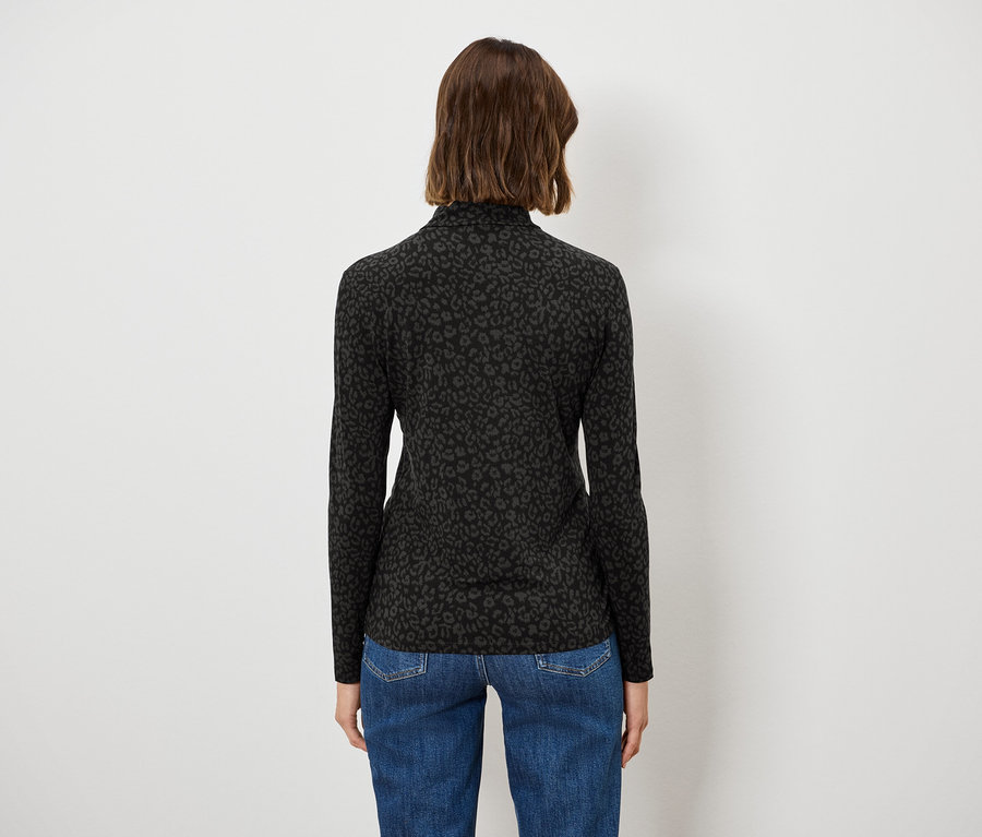 Frau steht mit dem Rücken zur Kamera, trägt einen schwarzen Rollkragenpullover und blaue Jeans.