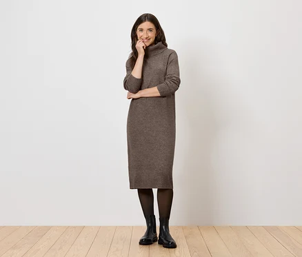 Frau posiert in einem braunen Rollkragenkleid, einer schwarzen Strumpfhose und Stiefeln.