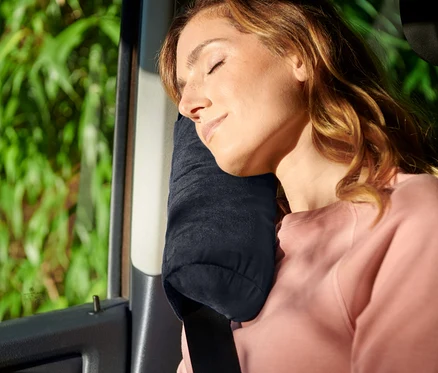 Frau schläft mit Nackenkissen im Auto, Sicherheitsgurt angelegt.