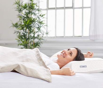 Frau liegt im Bett auf einem Medisana-SleepWell-Kissen »SP 100« mit Soundsystem und lächelt.