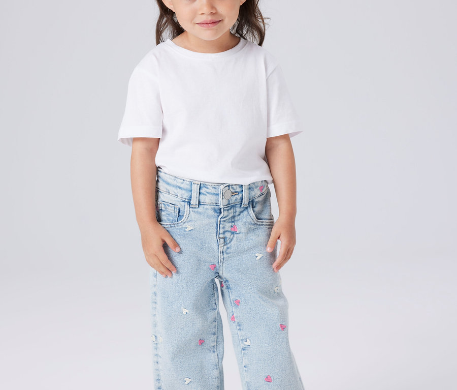 Mädchen mit weißem T-Shirt und hellblauen Jeans mit Herz- und Mausmuster.