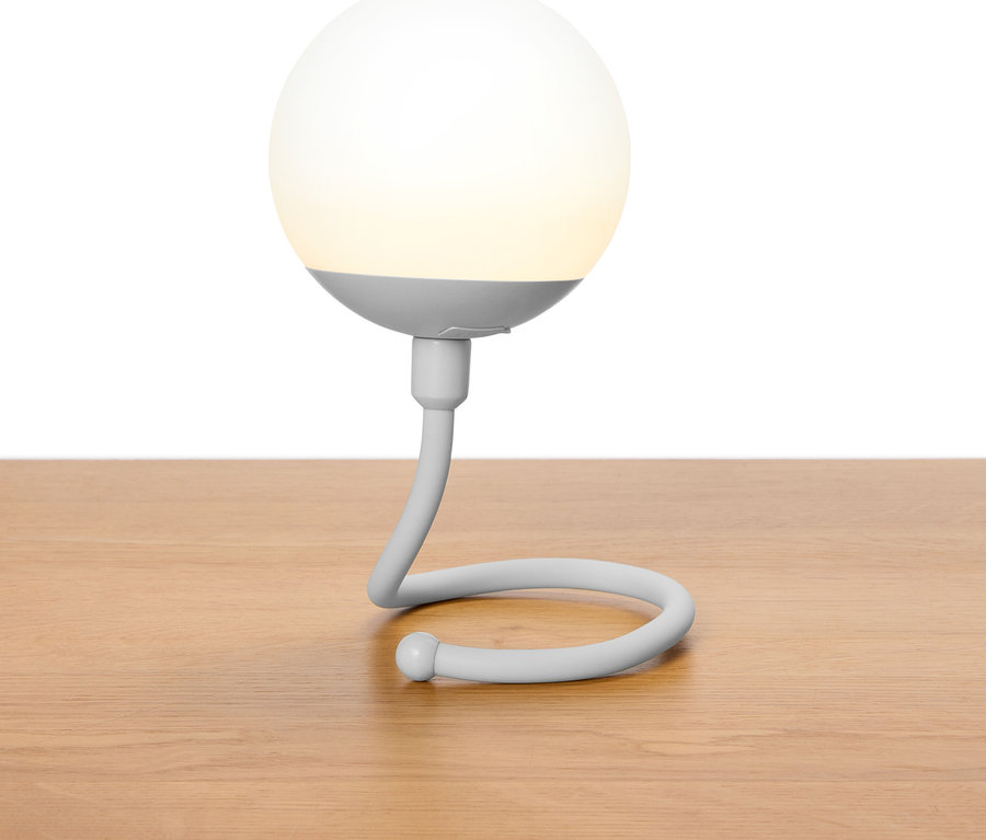 Graue kugelförmige Lampe mit geschwungenem Hals steht auf einem Holztisch.