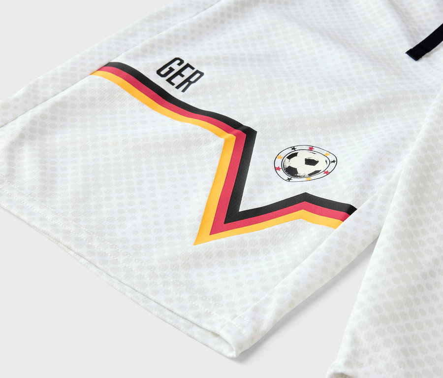 Nahaufnahme eines weißen Fußballtrikots mit den Farben der deutschen Flagge am Ärmel und der Abkürzung 'GER'.