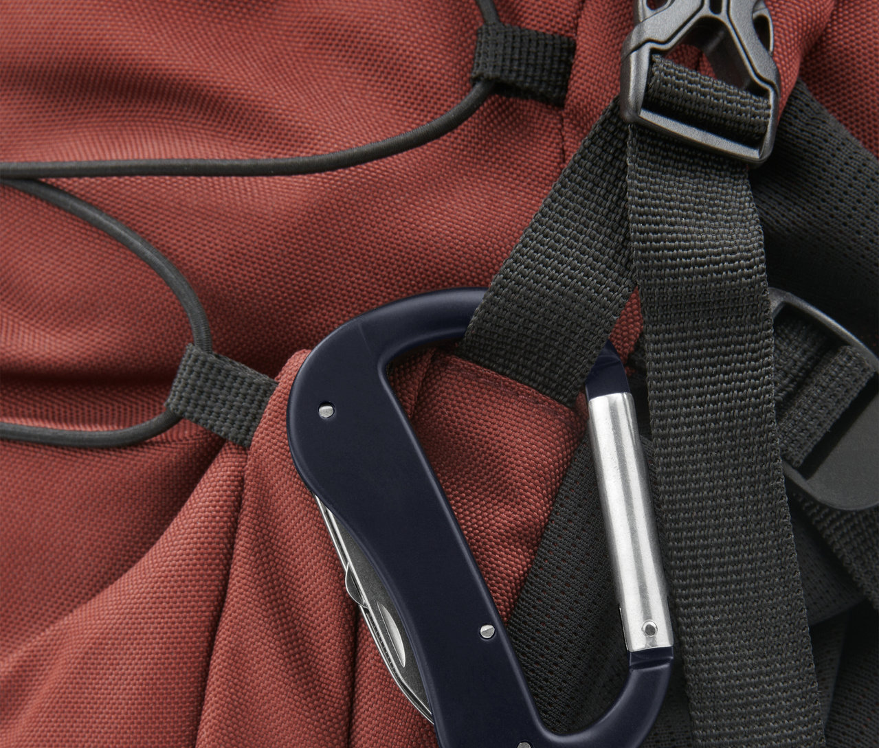 Nahaufnahme eines Karabinerhakens mit einem Multitool, befestigt an einem roten Rucksack.