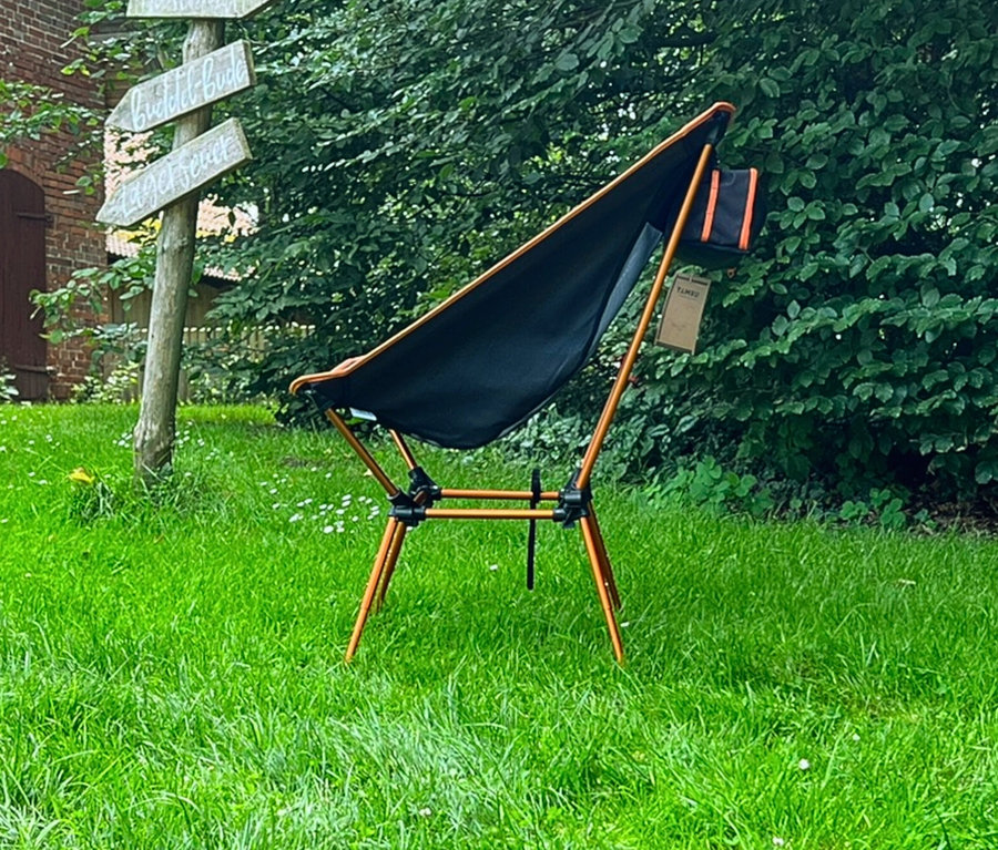 Der Tambu Campingstuhl »BATASA COMFORT« steht auf einer grünen Wiese vor Bäumen und einem Wegweiser.