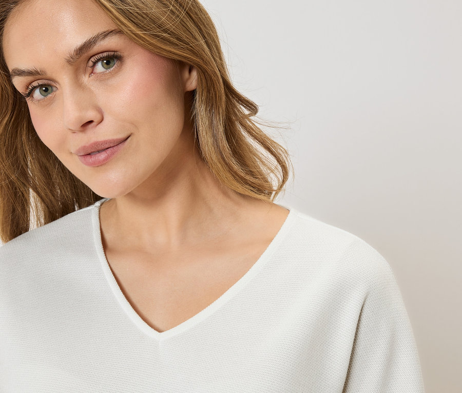 Porträt einer Frau mit blonden Haaren, die einen weißen Pullover mit V-Ausschnitt trägt.