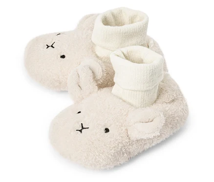 Nahaufnahme von zwei flaumigen, cremefarbenen Baby-Hausschuhen mit Hasengesicht und weißen Socken