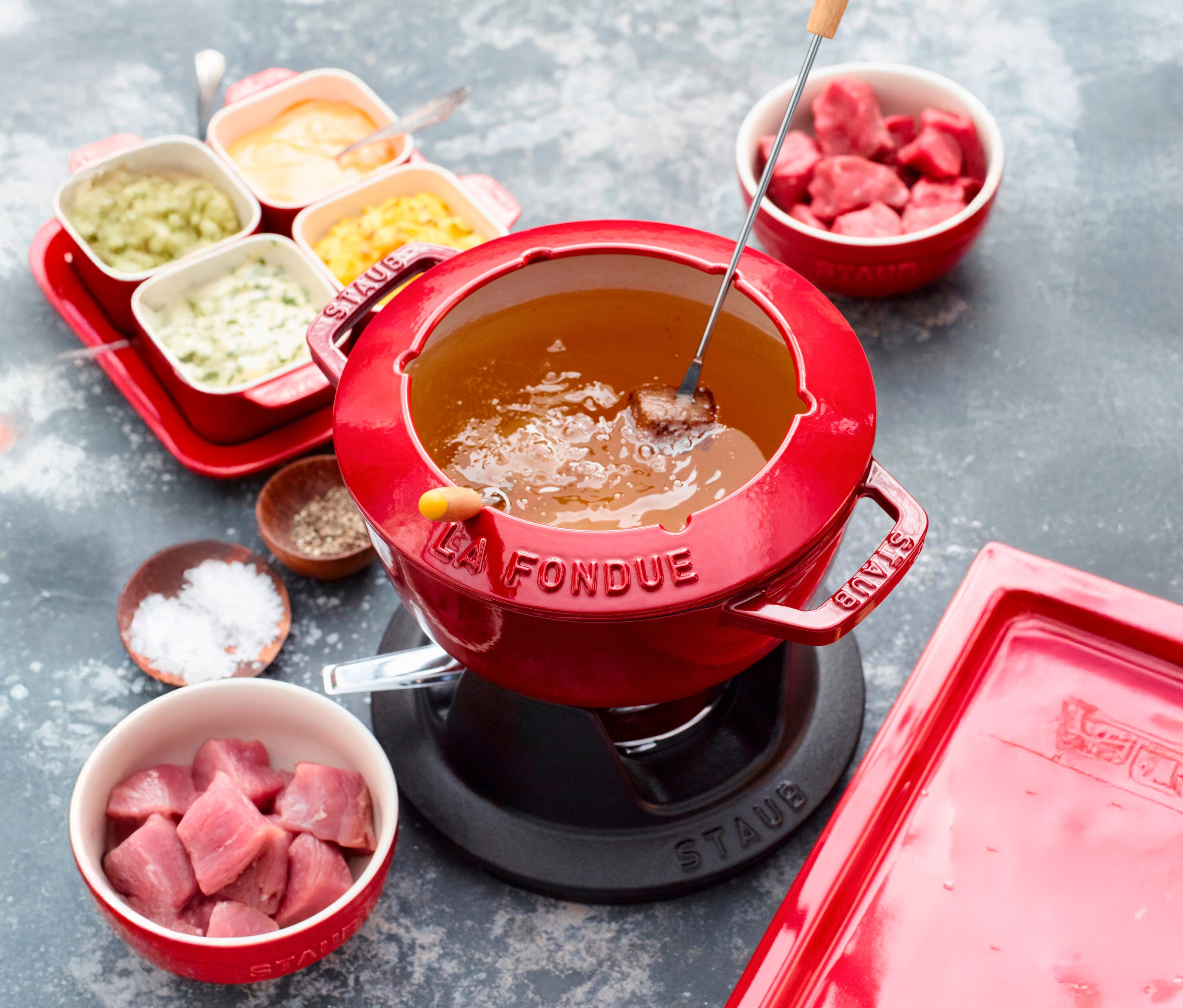 Rotes STAUB Fondue-Set mit Fleischstücken, Saucen und Gewürzen.