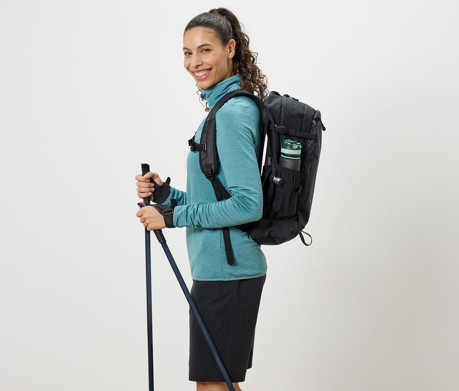 Frau mit türkisfarbenem Rollkragenpullover, schwarzem Rucksack und Wanderstöcken.