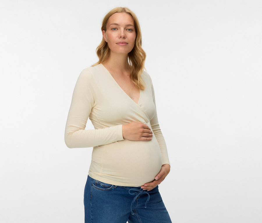 Schwangere Frau mit beigem MAMALICIOUS 2er Pack Top »MLKERRIE« und Jeans, die ihren Bauch hält.