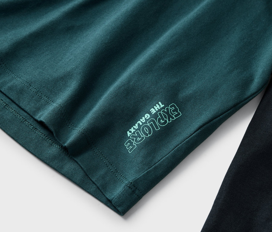 Nahaufnahme eines dunkelgrünen T-Shirts mit der Aufschrift "Explore the Galaxy" neben einer schwarzen Hose.